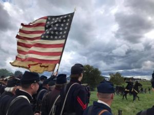 A back view of actors in uniform holding the American Flag reenacting the history